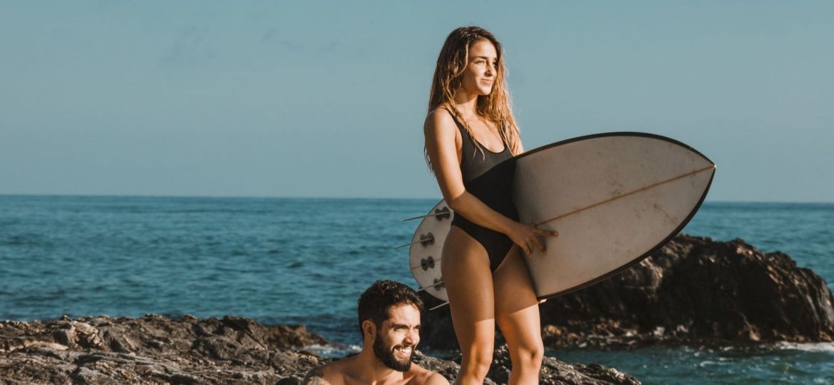 young-smiling-man-woman-with-surf-boards-rock-near-sea